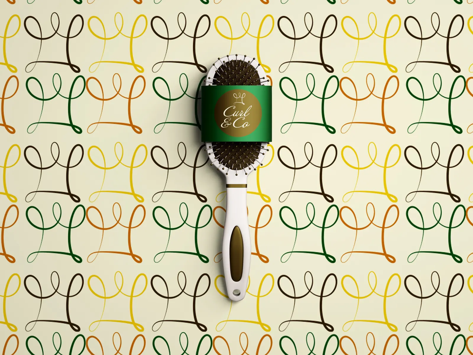 A white hairbrush wrapped in a green Curl & Co. band, lying on the brand's pattern of looping curl marks in brown, green, orange and yellow on cream