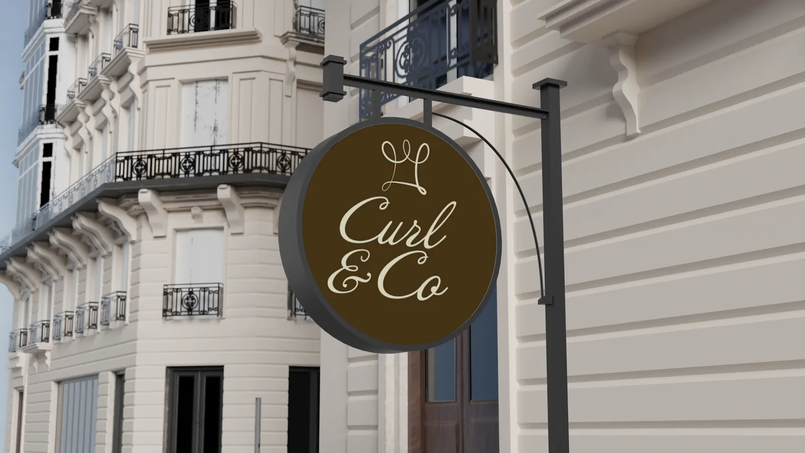 Round hanging shop sign with the cream Curl & Co. logo on dark brown, mounted on a building with wrought-iron balconies